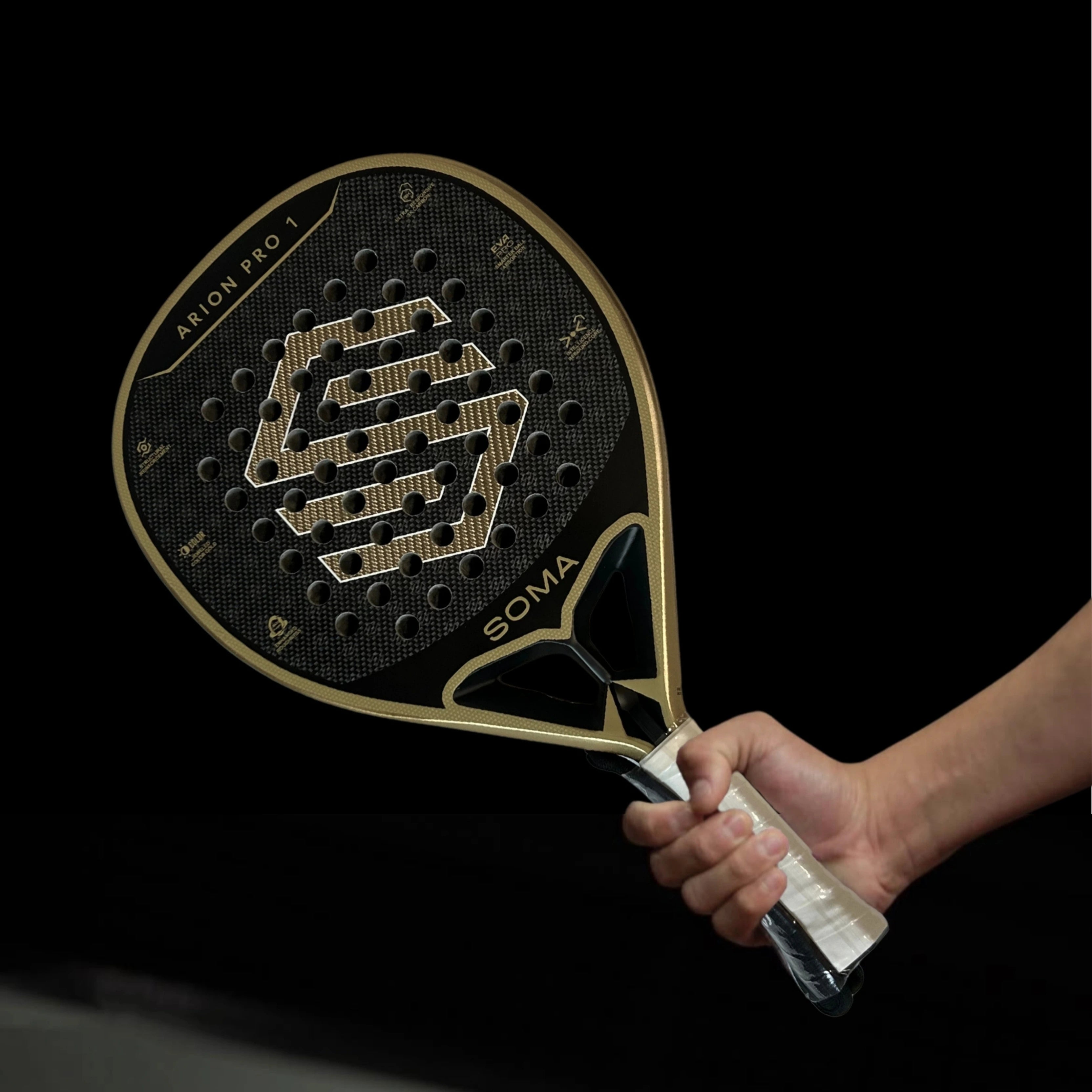 Raquette de padel Soma Arion Pro 1 noire et dorée tenue à la main  grip blanc et logo visible